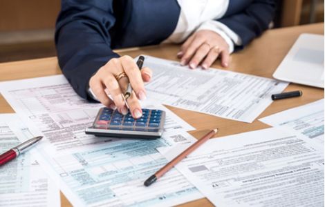 Consulenza fiscale e amministrativa per aziende negli USA - L'immagine mostra una professionista in giacca elegante che utilizza una calcolatrice e compila documenti fiscali ufficiali su una scrivania. Penne e fogli compilati evidenziano l'attenzione ai dettagli nella gestione delle tasse e delle pratiche burocratiche. Us Company Advisor assiste le aziende italiane nell'apertura e gestione fiscale di società negli Stati Uniti, garantendo conformità alle normative americane.