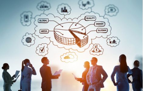 Un gruppo di professionisti d'affari in controluce discute strategie aziendali davanti a un grafico concettuale digitale. Il grafico include una rappresentazione a torta con parole chiave come 'Global', 'Quality', 'Design', 'Slogan' e 'Media', collegate da nuvole concettuali. L'immagine evoca innovazione, networking e sviluppo aziendale internazionale.