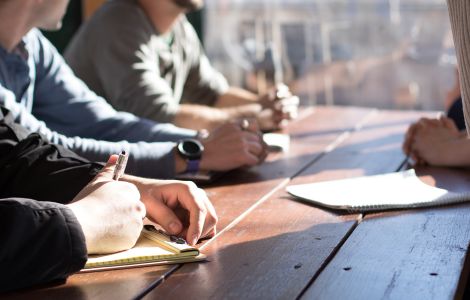 Servizio di ufficio stampa e comunicazione aziendale negli USA - L'immagine mostra un gruppo di professionisti seduti attorno a un tavolo con blocchi per appunti e penne, impegnati in una riunione strategica. La scena rappresenta la pianificazione di comunicati stampa, strategie di PR e gestione dei media. Us Company Advisor offre servizi di ufficio stampa per aziende italiane, curando la visibilità e la reputazione nel mercato statunitense.